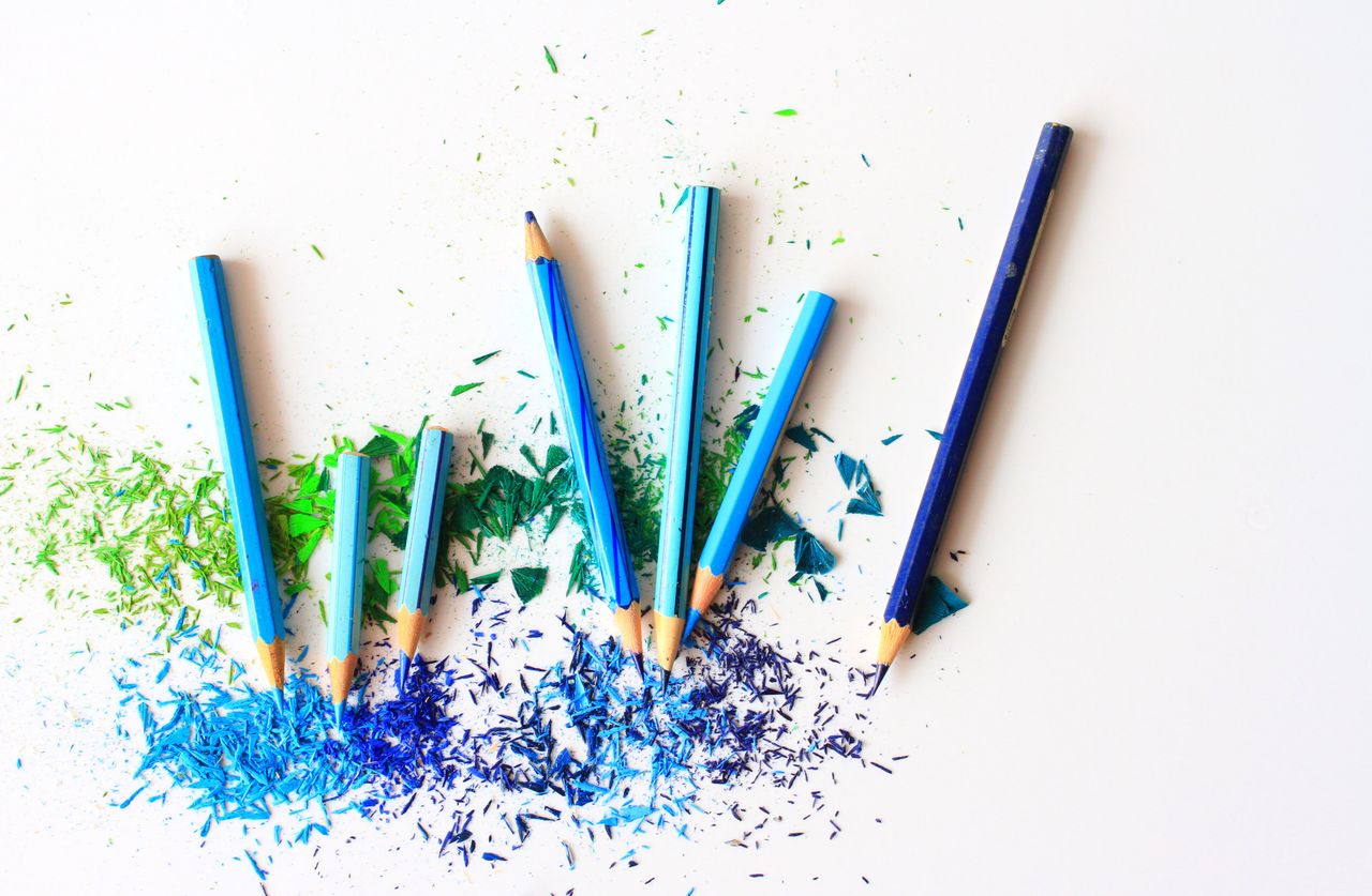 our-story Creative display of colored pencils and vibrant shavings on a white background.